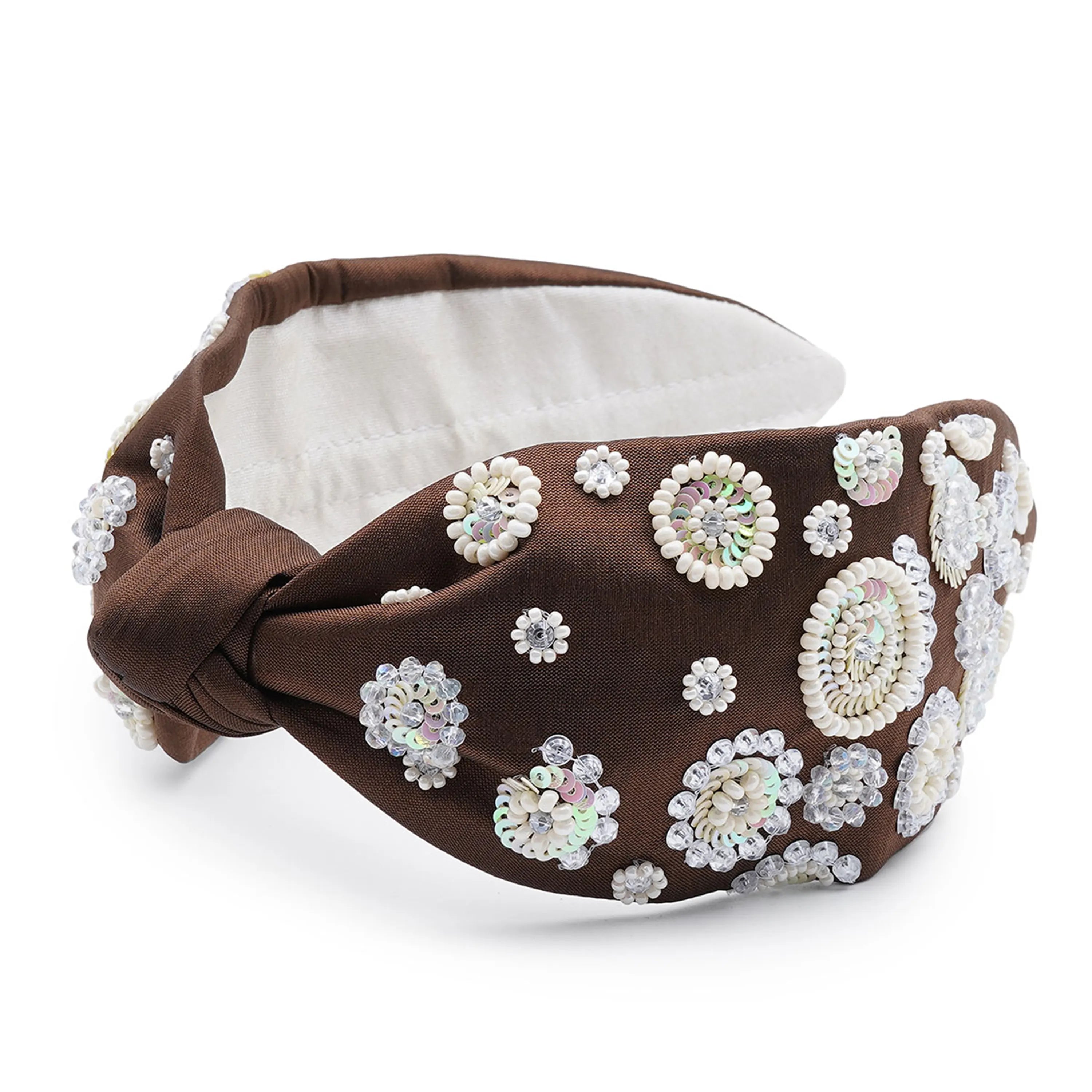 A brown satin headband with a white fabric top decorated with a vintage floral circle pattern embellished with rhinestones.